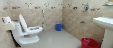 A bathroom with a toilet, bidet, sink, and a blue and red bucket.