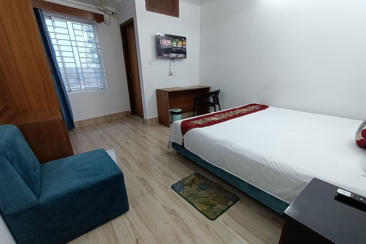 A hotel room with a bed, a desk, a chair, a TV, and a window with bars.