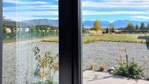 A view through a window of a rural landscape with mountains in the distance, a clear sky, and a gravel path.