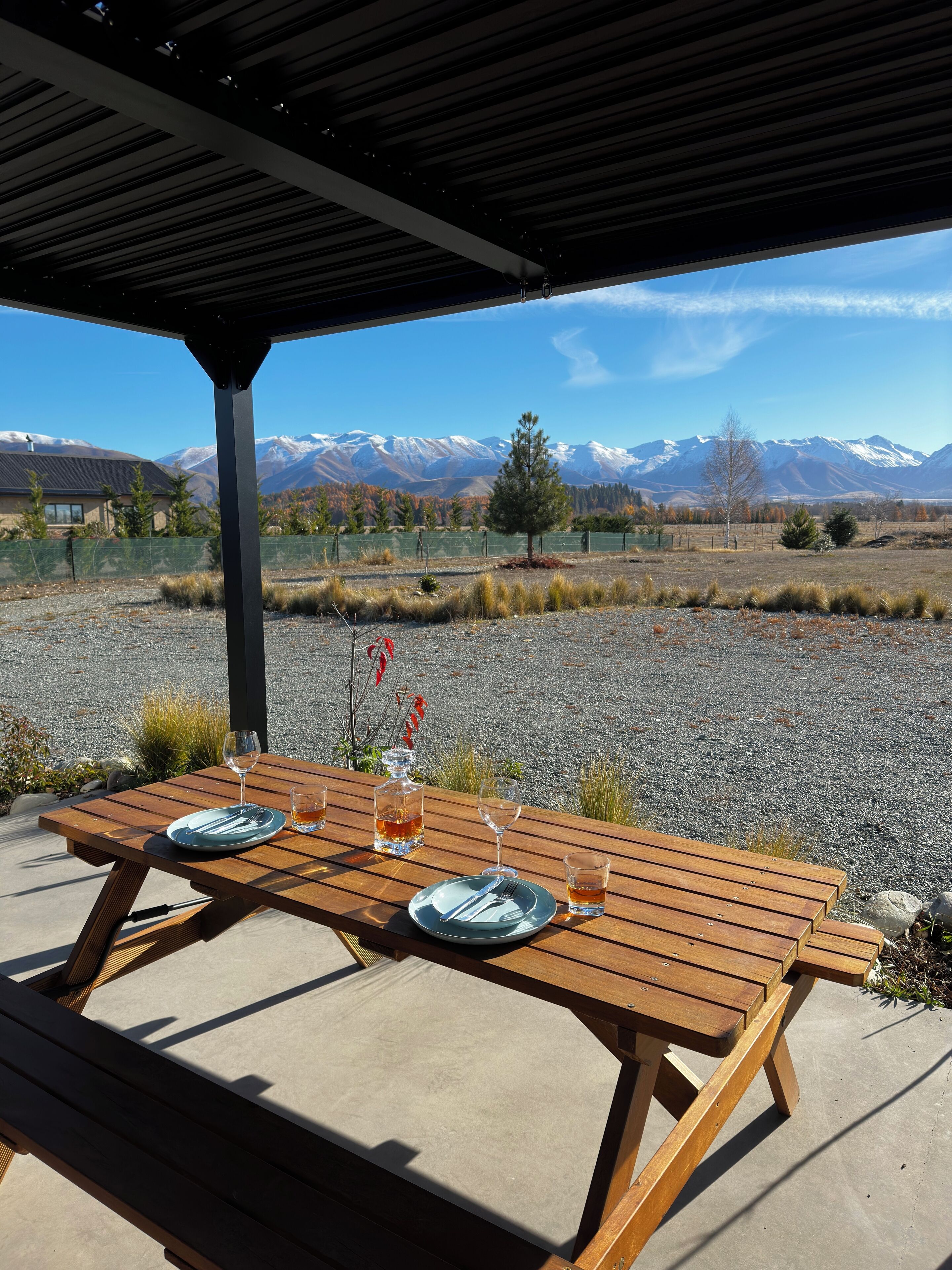 A wooden picnic table with plates, cutlery, and glasses set outdoors, overlooking a mountainous landscape.