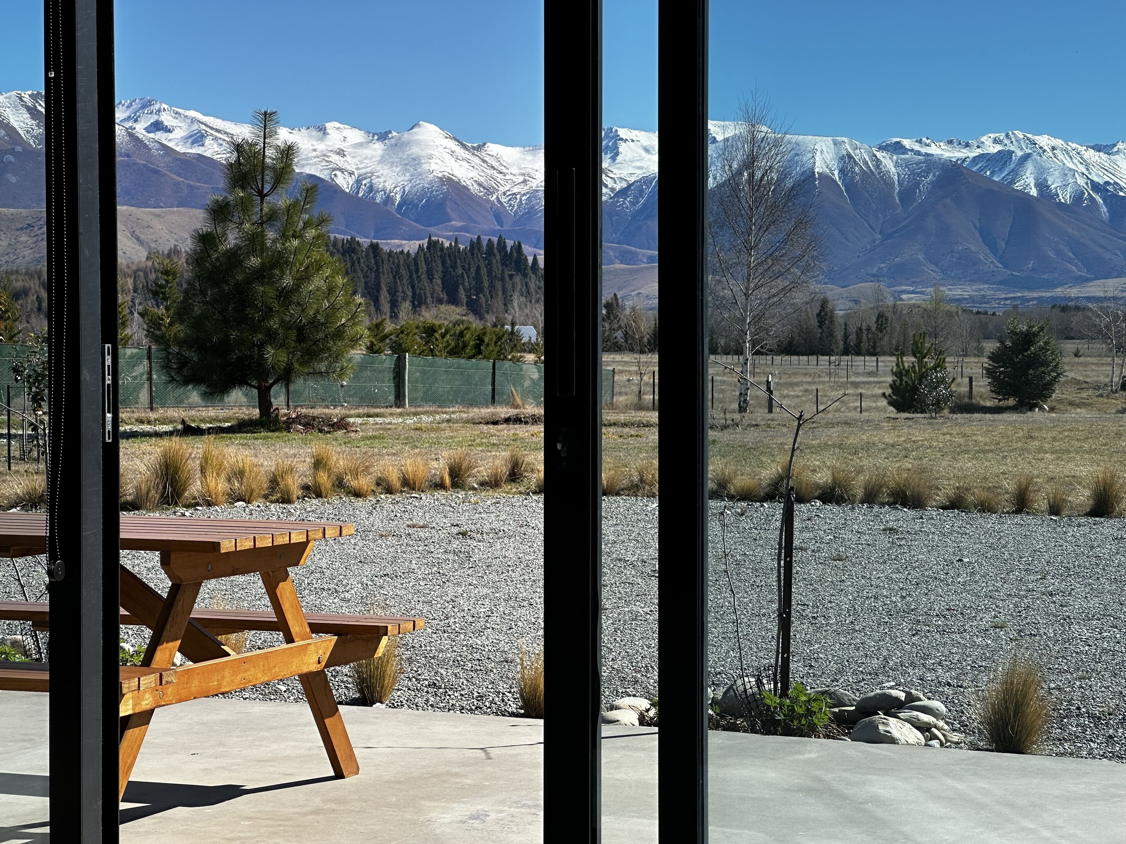 A wooden picnic table with a view of snow-capped mountains through a window.