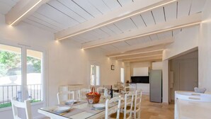 Un grand espace à manger avec une table en verre, des chaises blanches et une cuisine en arrière-plan.