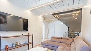 Un salon moderne avec un canapé d’angle, un téléviseur à écran plat et un escalier menant à un autre niveau.