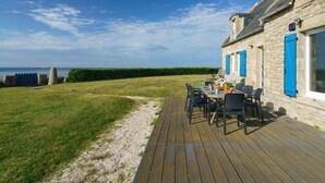 Ein Steinhaus mit blauen Fensterläden, einer Holzterrasse und einem Tisch mit Stühlen.