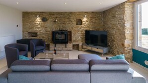 Ein modernes Wohnzimmer mit Kamin aus Stein, einem Flachbildfernseher und bequemen Sitzmöglichkeiten.