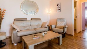 A living room with a sofa, two armchairs, a coffee table, a floor lamp, and a mirror on the wall.