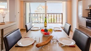 A dining area with a table set for four, a bottle of wine, and a bowl of fruit.