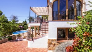 Uma casa de dois andares com piscina, varanda coberta e fachada de pedra.