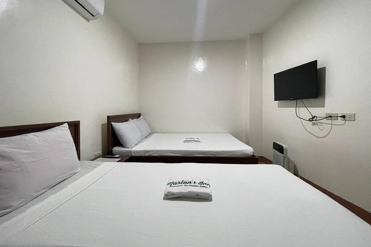 A hotel room with two single beds, a flat-screen TV mounted on the wall, and an air conditioning unit on the ceiling.