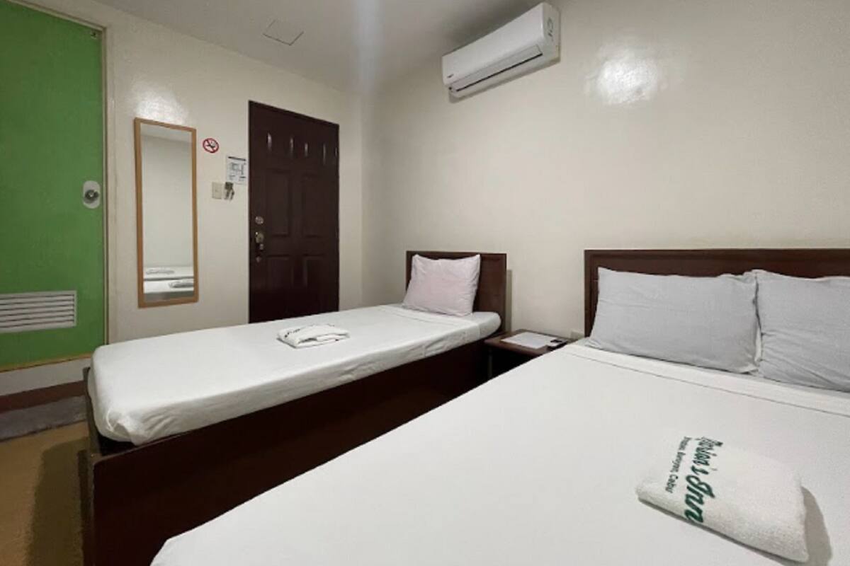 A hotel room with two single beds, a green door, a white air conditioner, and a mirror on the wall.