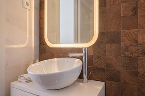 Ein Badezimmer mit einem weißen Waschtischbecken, einem Spiegel mit Beleuchtung und einer Holzvertäfelung.