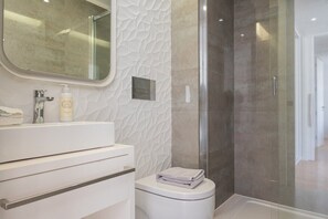 A modern bathroom with a white vanity, a glass shower enclosure, and a toilet with a towel on top. - COMFY PORTO - Charming flat with terrace located in Porto centre (Porto)