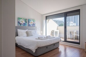 A modern bedroom with a large bed, two paintings on the wall, and a sliding glass door leading to an outdoor area. - COMFY PORTO - Charming flat with terrace located in Porto centre (Porto)