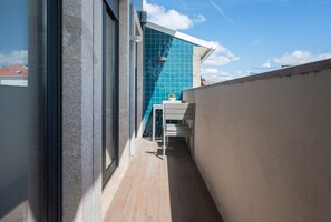 A narrow balcony with a view of a building with blue-tiled facade, a small table with a chair, and a potted plant. - COMFY PORTO - Charming flat with terrace located in Porto centre (Porto)