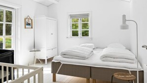 Une chambre à coucher comprenant un lit, une table de chevet, une chaise, une armoire et une fenêtre donnant sur un paysage verdoyant.