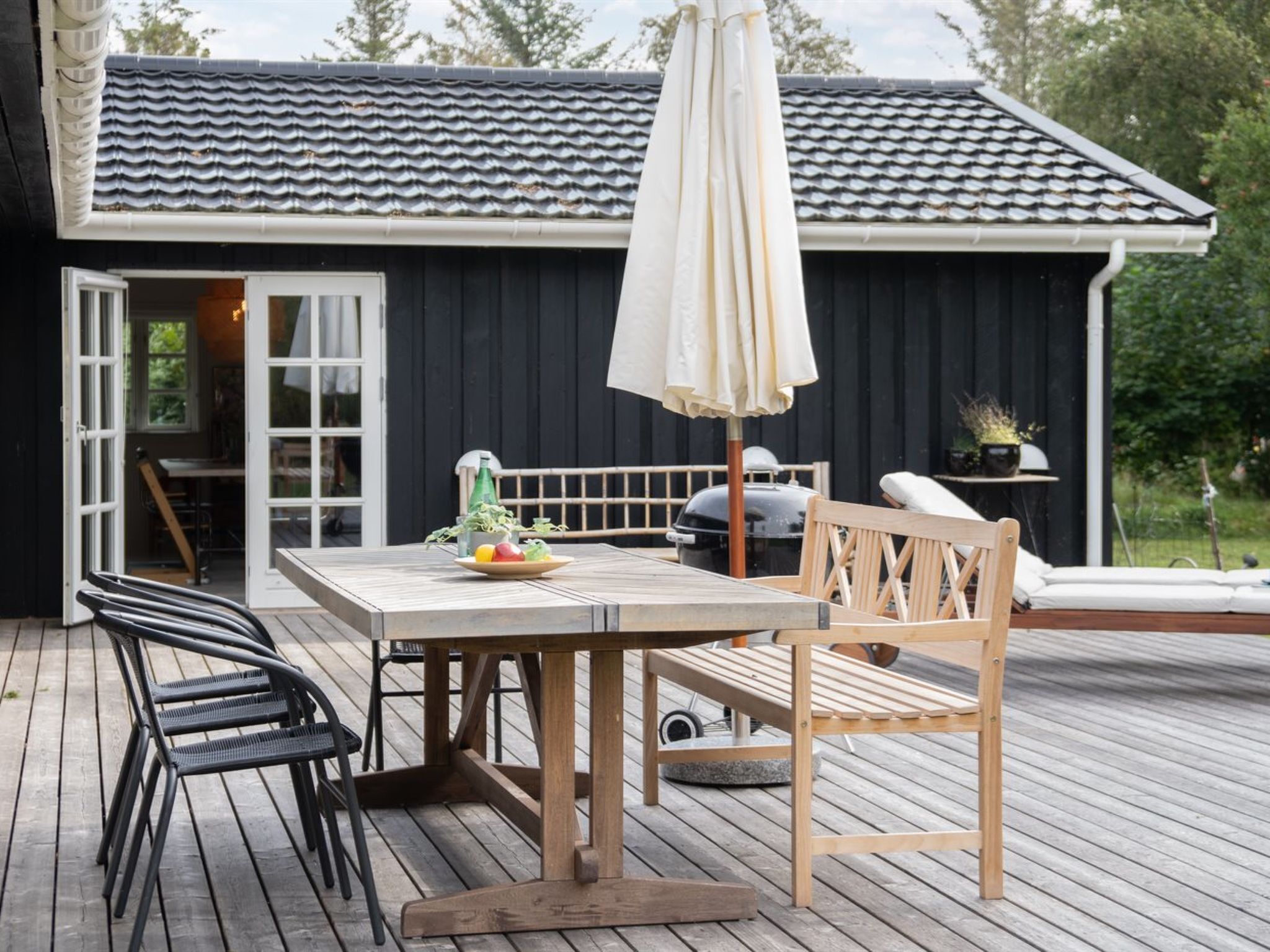 En träaltan med ett bord och stolar, en grill och en krukväxt.
