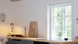 Une cuisine avec un plan de travail en bois, une horloge, une planche à découper et une fenêtre donnant sur un paysage verdoyant.