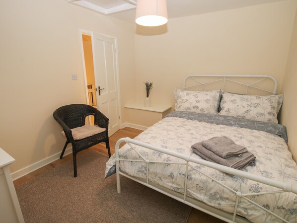 Ein Schlafzimmer mit Bett, Stuhl, kleiner Ablagefläche und Tür.