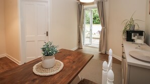 Una habitación con una mesa de comedor de madera, una puerta blanca y vistas a un patio exterior con plantas y una silla.