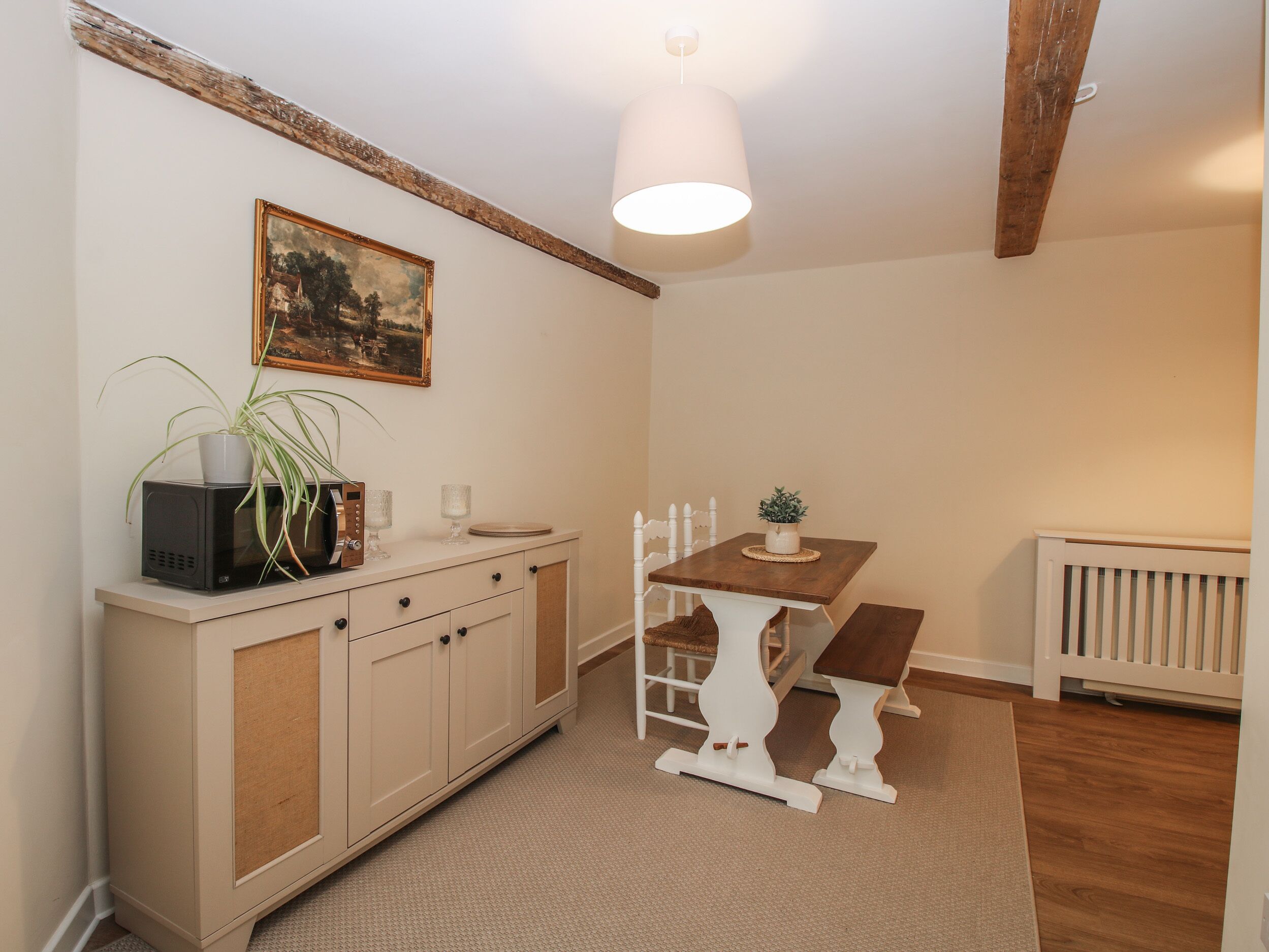 A small, cozy kitchen with a wooden table, a white cabinet, and a hanging light fixture.