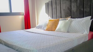 A neatly made bed with a patterned bedspread, a pillow with a solid color, and a headboard with a vertical panel design.