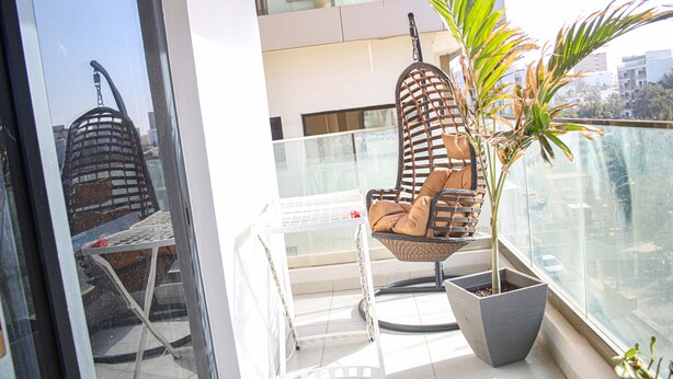 A balcony with a wicker chair, a potted plant, and a white metal table.