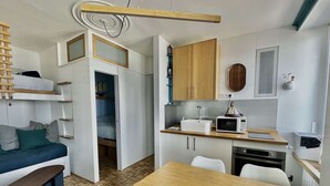 A compact living space with a kitchenette, a dining area, and a bed with a loft. - À L'est - Studio vue mer sur la Digue (Arromanches-les-Bains)