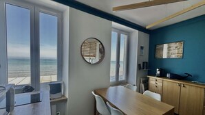 A modern kitchen with a view of the sea, a round mirror, and a wooden dining table with chairs. - À L'est - Studio vue mer sur la Digue (Arromanches-les-Bains)