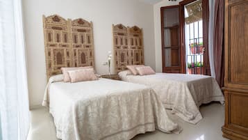 A hotel room with two beds, a decorative wall panel, a window with a view of flowers, and a wooden cabinet.