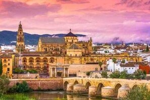 A historic building with a prominent tower and arches, located beside a river with a bridge. - Mezquita House Free Parking (Cordoba)