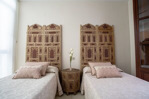 Una habitación con dos camas, una mesita redonda con un florero y elaborados cabeceros de madera.