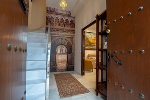 Un pasillo con una escalera de mármol, un tapiz con diseño y una puerta de madera con picaporte de latón.