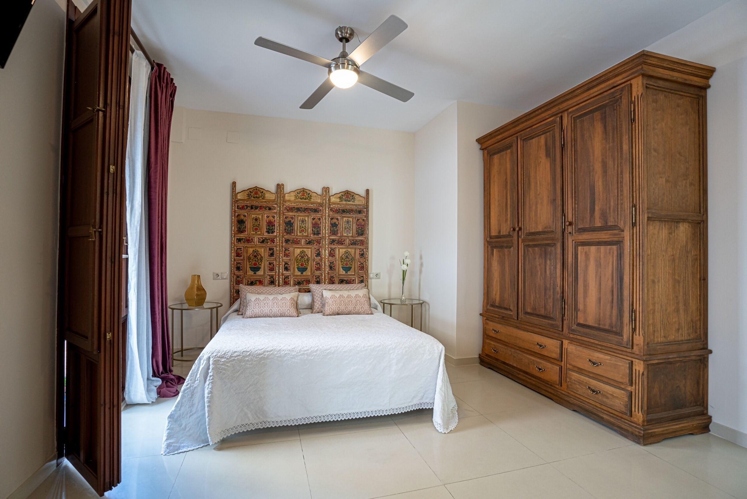 A bedroom with a bed, a wardrobe, a ceiling fan, and a decorative headboard.