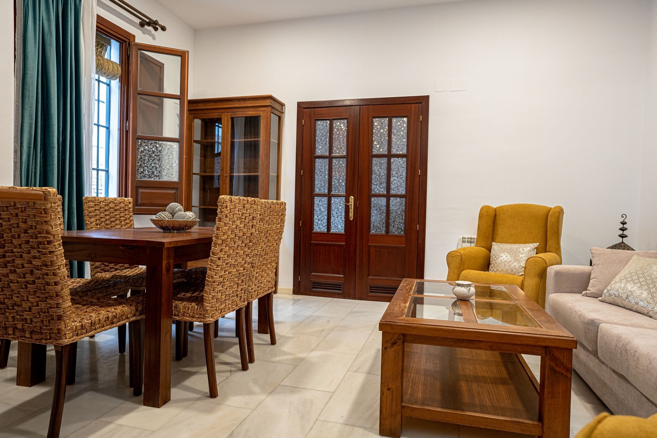 Un comedor con sillas de mimbre, una mesa de madera y una mesa de centro con cubierta de vidrio.
