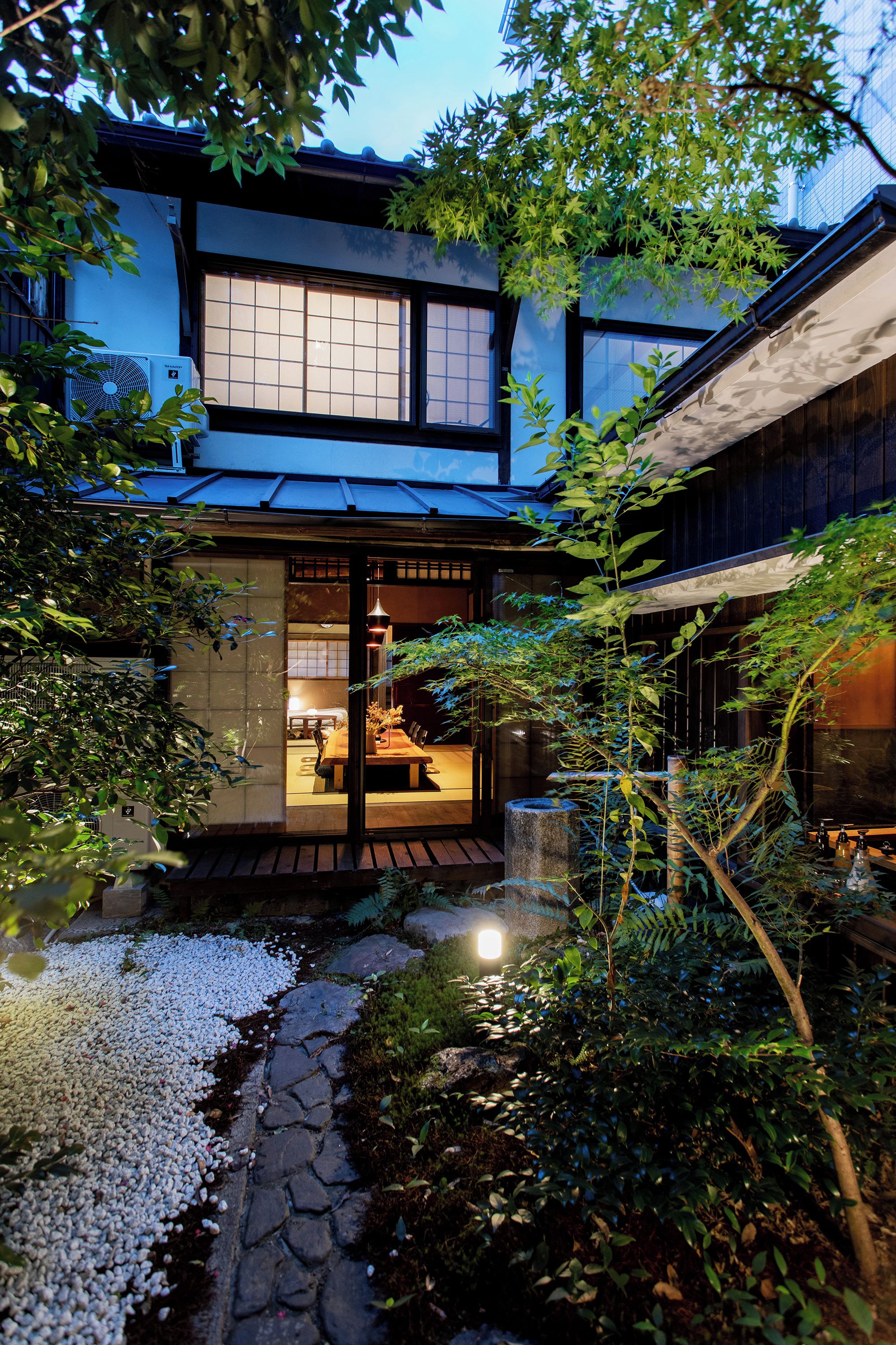 Una casa tradicional japonesa amb un camí de jardí que condueix a una zona de menjador de fusta.