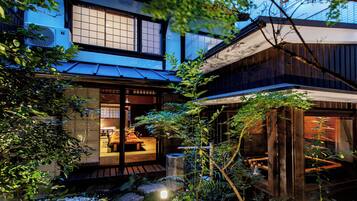 Una casa tradicional japonesa amb façana de fusta, un espai interior amb esteimat i un camí de pedra que condueix a l'entrada.