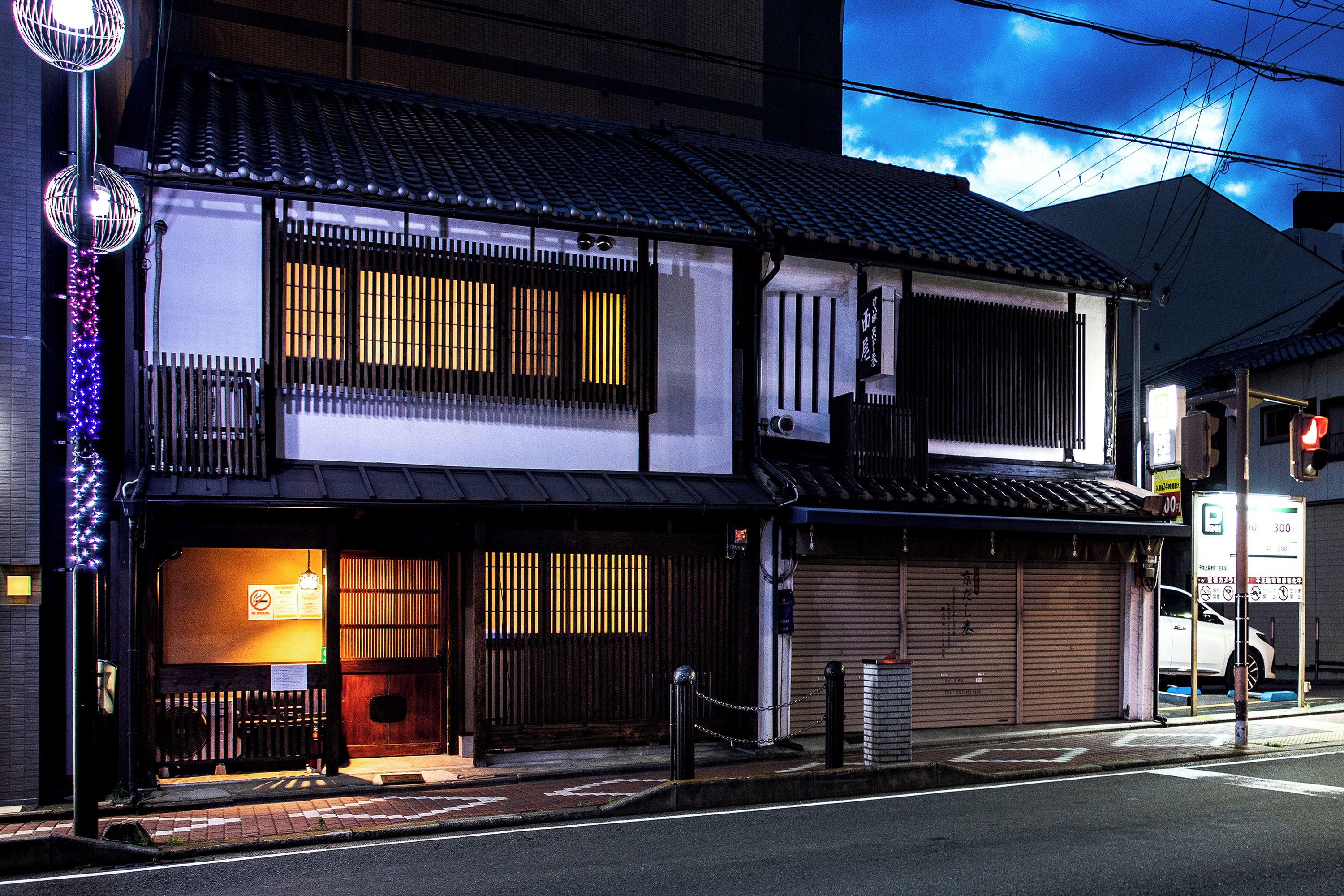 Edifici tradicional japonès amb una estructura de dos pisos, grans finestres i una porta de garatge visible.