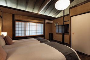 Una habitación de hotel con suelo de tatami, un amplio ventanal con pantalla shoji, un televisor de pantalla plana y una cama de estilo japonés tradicional.