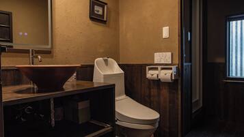 A bathroom with a wooden floor, a sink with a mirror, a toilet, and a framed picture on the wall.