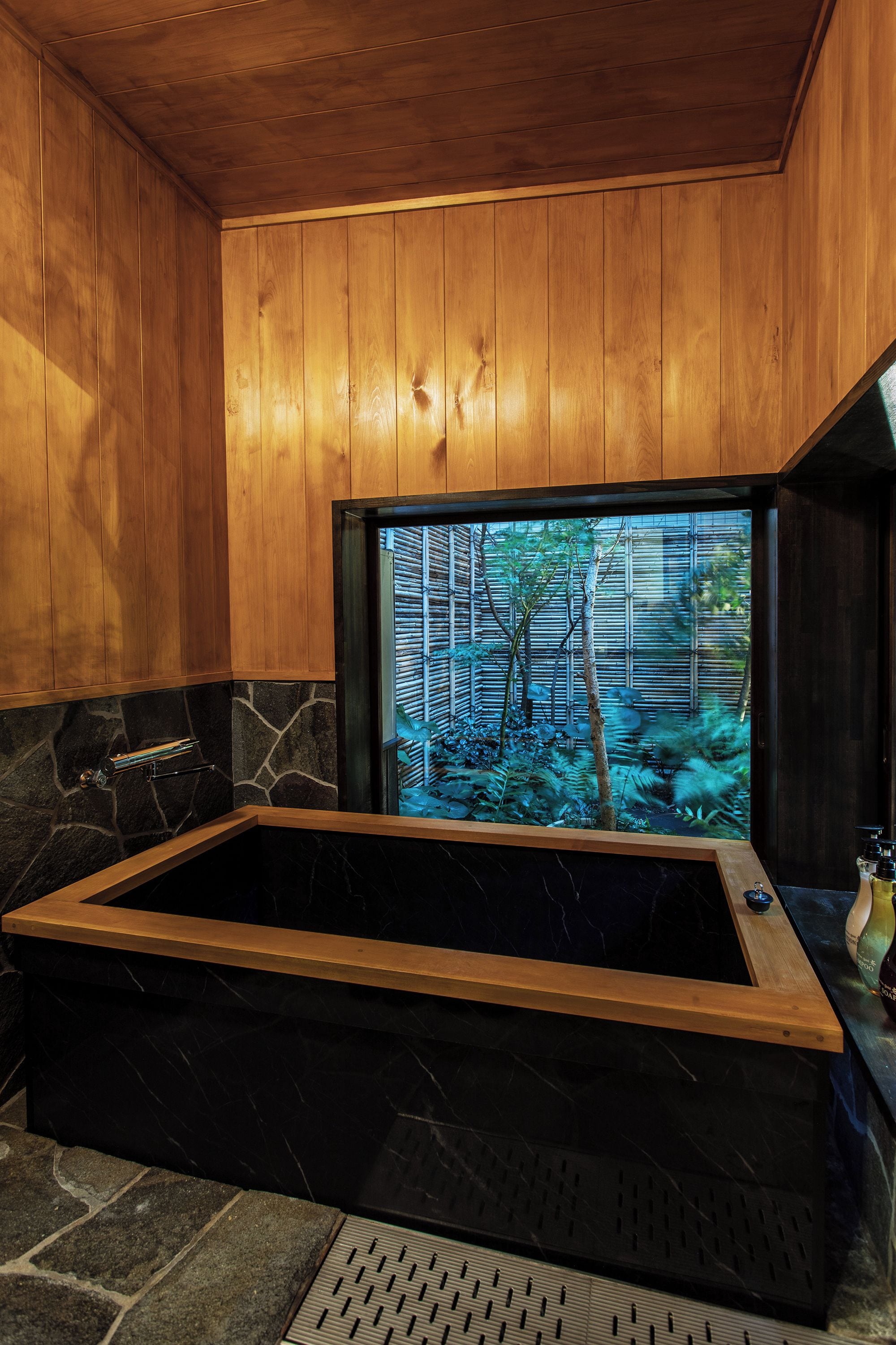 Interior de madera con una bañera grande y vistas a un bosque de bambú a través de una ventana.