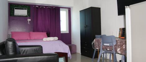 A bedroom with a bed, a desk, a chair, a wardrobe, and an air conditioner.