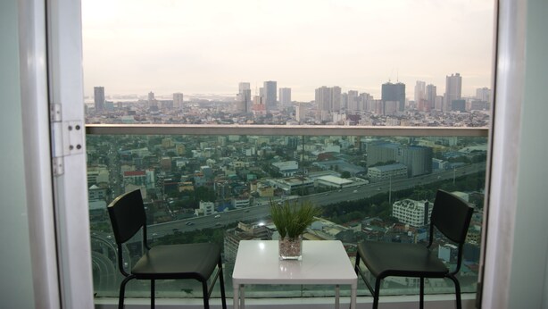 Un balcon avec deux chaises et une petite table, donnant sur un paysage urbain composé d’immeubles de grande hauteur et d’une autoroute.
