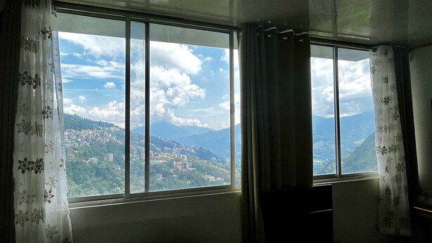 A room with a large window offering a view of a mountainous landscape. - The Hill Castle (Gangtok)