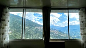A room with a large window offering a view of a mountainous landscape. - The Hill Castle (Gangtok)