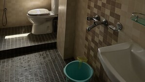 A bathroom with a toilet, shower, and bathtub. There is a window providing a view of buildings and mountains. - The Hill Castle (Gangtok)