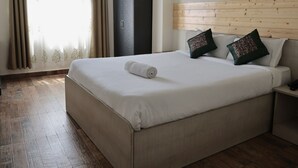 A hotel room with a large bed, wooden headboard, two patterned pillows, a nightstand, and a wardrobe. - The Hill Castle (Gangtok)
