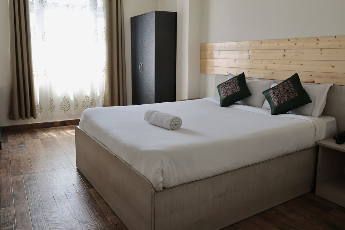 A hotel room with a large bed, wooden headboard, two patterned pillows, a nightstand, and a wardrobe.