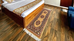 A bedroom with a wooden bed, a patterned rug, a wooden wardrobe, and a small bedside table. - The Hill Castle (Gangtok)