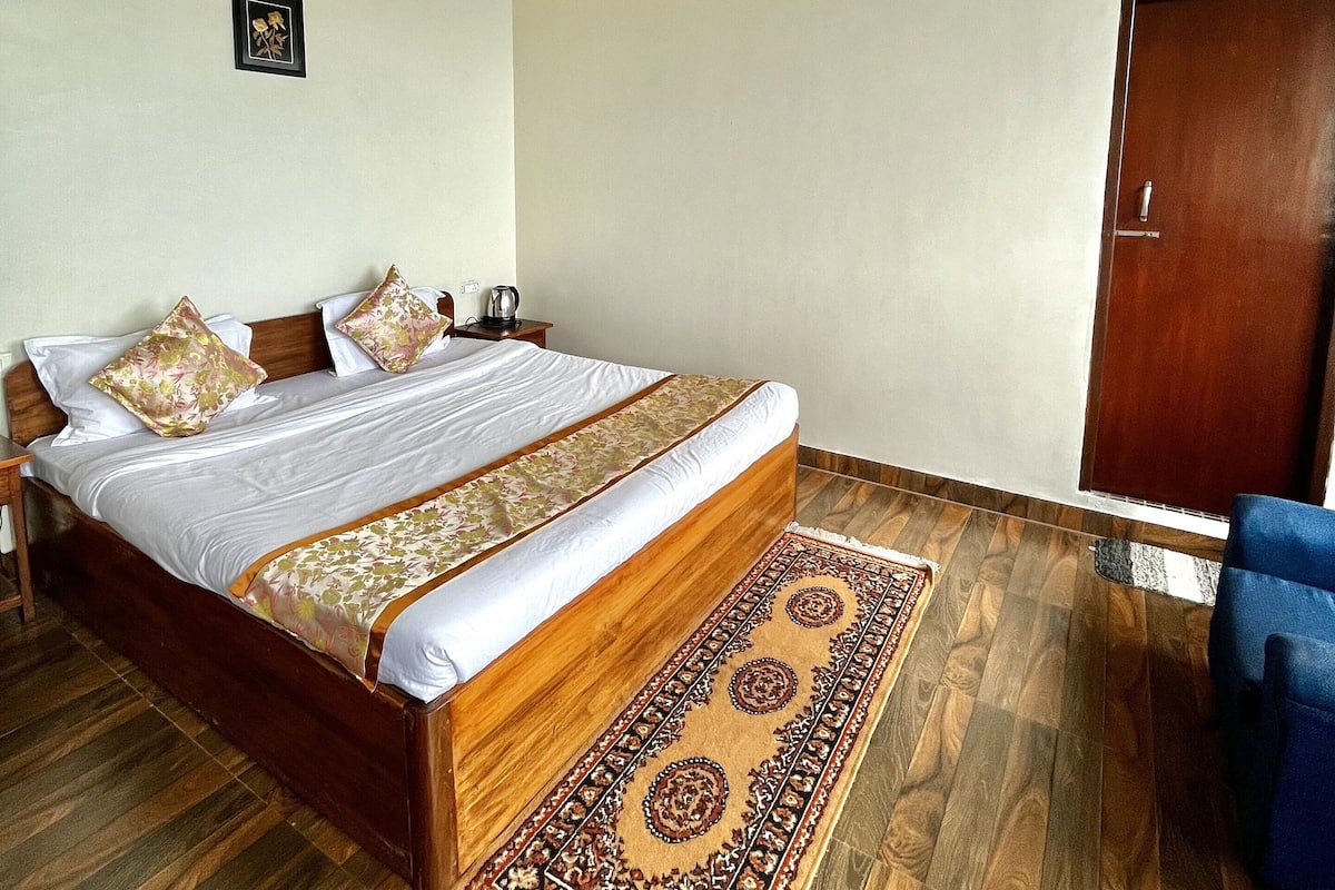 A bedroom with a wooden bed, a patterned rug, a wooden wardrobe, and a small bedside table.
