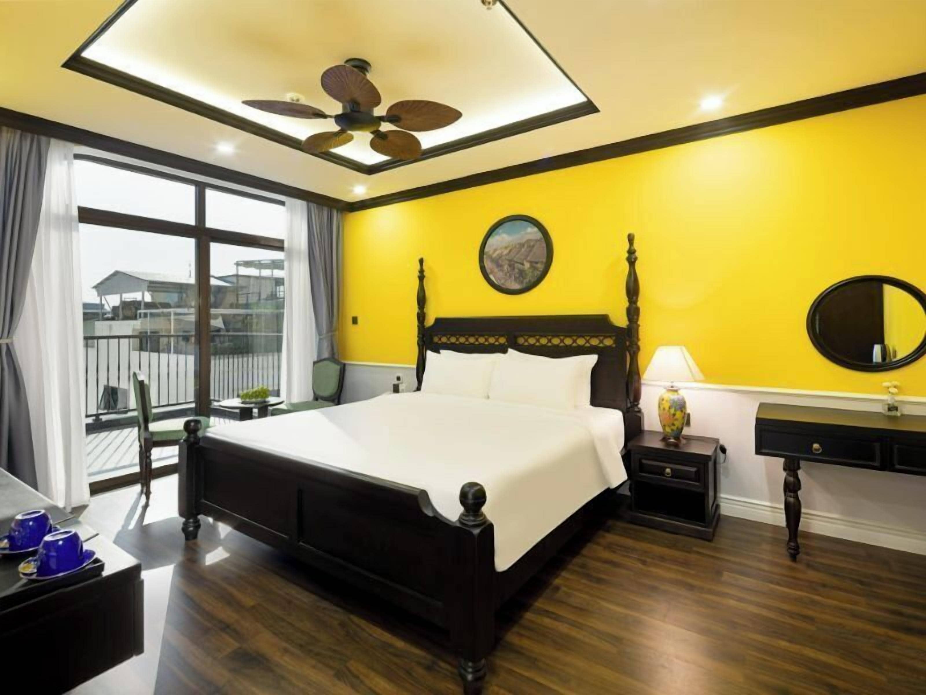 A hotel room with a large bed, a ceiling fan, a round mirror, and a view of the outdoors.